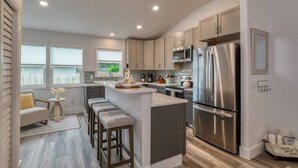 A modern kitchen with a central island, stainless steel appliances, and a view of the outdoors. - Aqua Palms Cottage (St. Augustine)