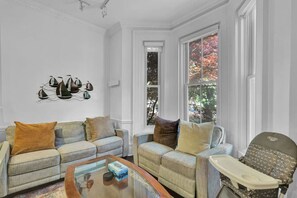 Un salon avec deux canapés, une table basse et un fauteuil. Une fenêtre donne sur le paysage automnal.