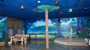An indoor stage with a painted backdrop of a forest and lake, a wooden bench, and a table. - Veluwemeer Chalet Park Retreat (Hulshorst)