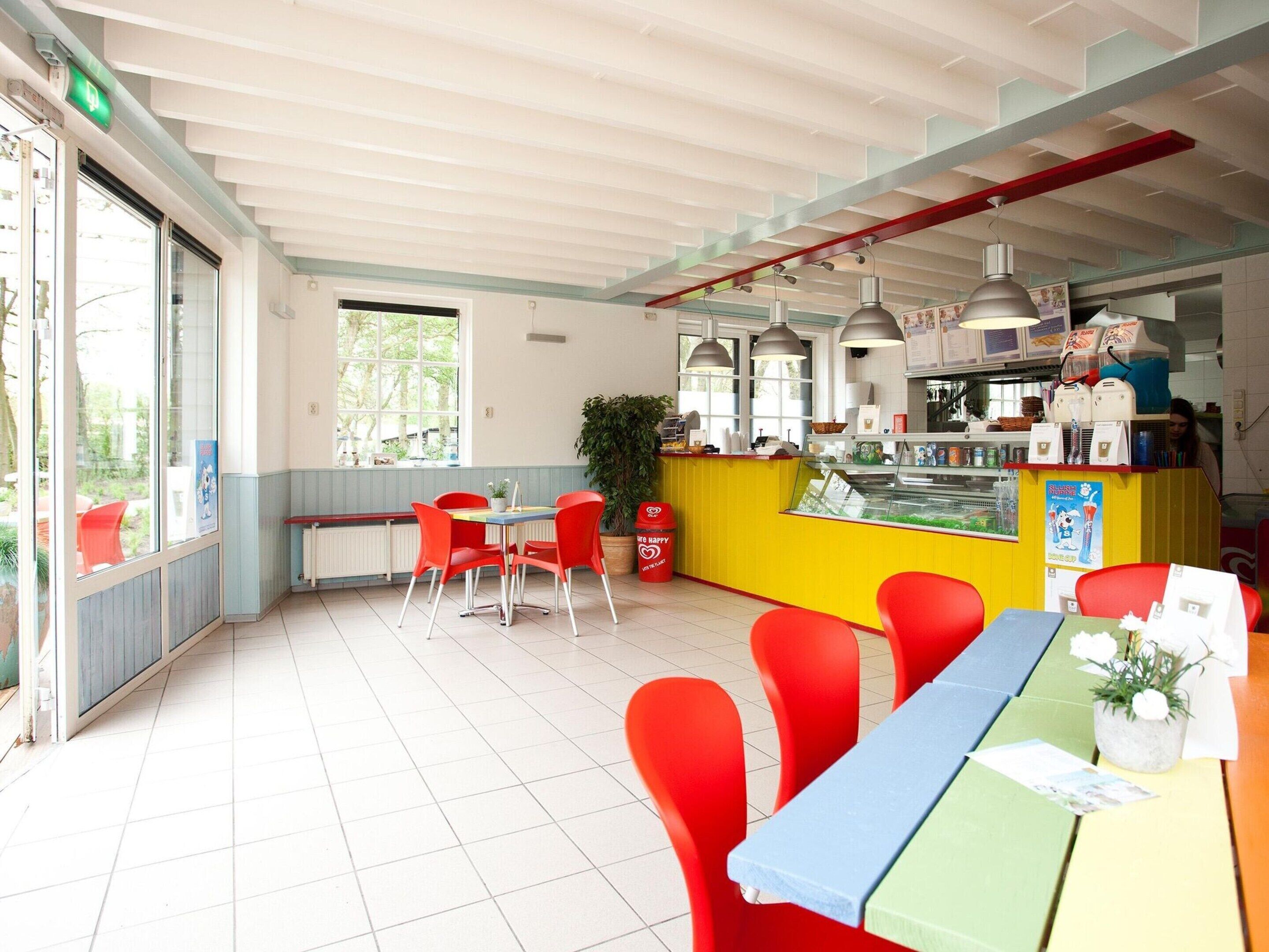 A brightly lit cafe with red chairs, a yellow counter, and a large window.