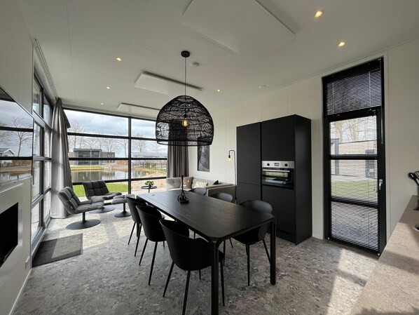 A modern kitchen with a dining area, large windows, and a built-in oven. - Veluwemeer Chalet Park Retreat (Hulshorst)