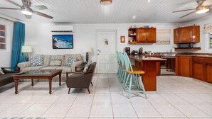 A spacious living room with a sofa, chairs, a coffee table, and a kitchen area with wooden cabinets and appliances. - Ideal Home for Larger Family with Pool in Noord (Noord)