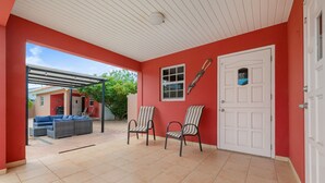 A covered patio area with tiled flooring, a white door, and two striped chairs. - Ideal Home for Larger Family with Pool in Noord (Noord)