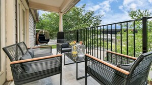 A balcony with outdoor furniture, a grill, and a glass table.