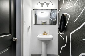 Casa de banho com lavatório branco, espelho e parede preta com desenhos abstratos em branco.