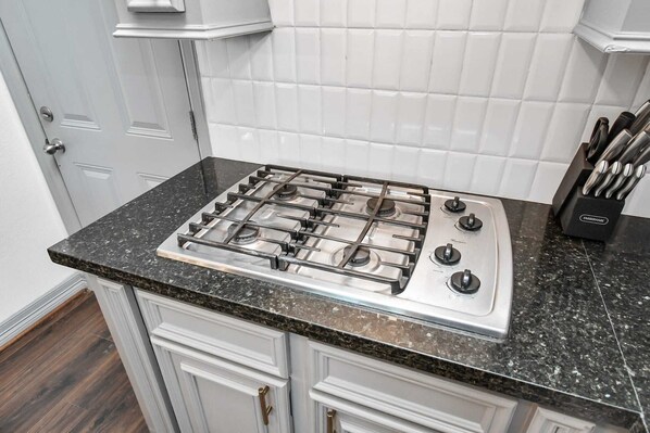 A kitchen with a gas stove, white cabinets, and a knife block.