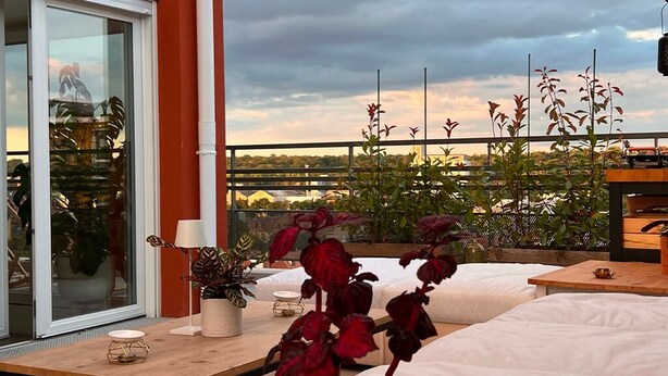 A modern outdoor seating area with a view of the city skyline, a glass door entrance, and potted plants. - Duplex de la Gare, Rooftop, Jacuzzi (Corbeil-Essonnes)