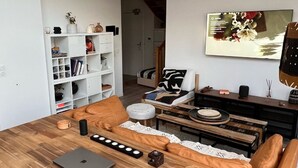 A modern living room with a wooden dining table, leather sofa, and a white shelving unit. - Duplex de la Gare, Rooftop, Jacuzzi (Corbeil-Essonnes)