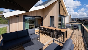 A modern house with a wooden deck, a dining area, and a large sliding glass door. - Villa in Breskens Near the Beach (Breskens)