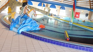 An indoor swimming pool with a dolphin sculpture, a wooden ceiling, and a red flag. - Villa in Breskens Near the Beach (Breskens)
