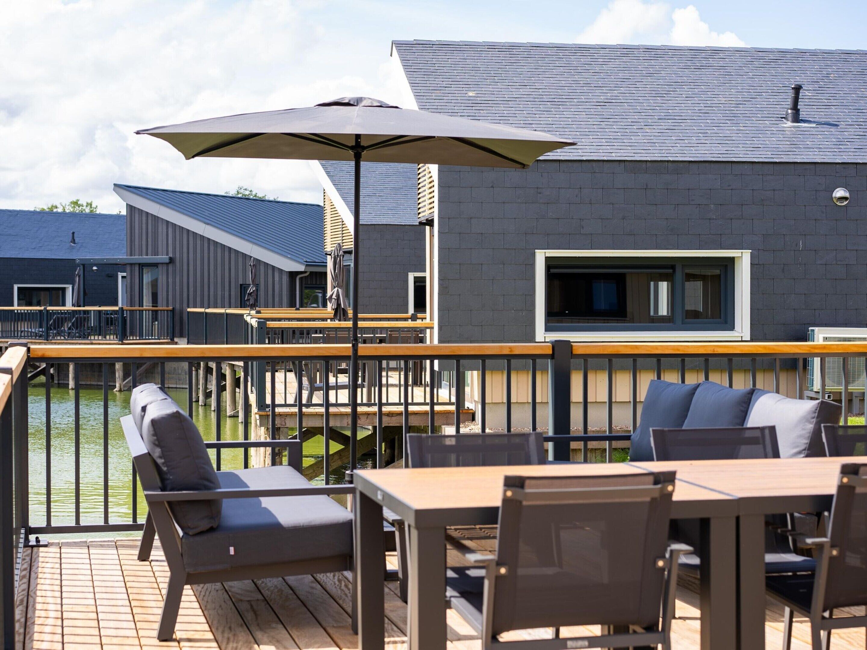 A deck with outdoor seating, a large umbrella, and a view of a building with a window and a chimney.
