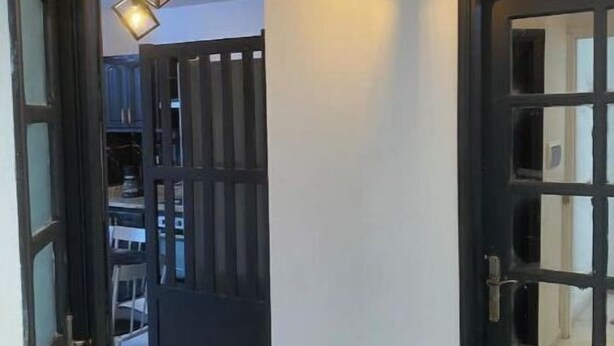 Corredor com porta preta e parede branca. Duas luminárias pendentes com lâmpadas aparentes.
