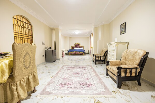 Une pièce spacieuse avec un grand lit, un coin salon comprenant un fauteuil et une table, ainsi qu’un tapis décoratif.