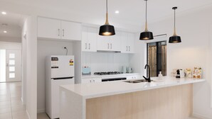 Una cocina moderna con armarios blancos, una isla central, lámparas colgantes negras y un lavamanos de acero inoxidable.