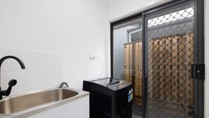 Una cocina con un lavamanos de acero inoxidable, un lavavajillas negro y un ventanal corredizo que da a un espacio exterior con valla de madera.