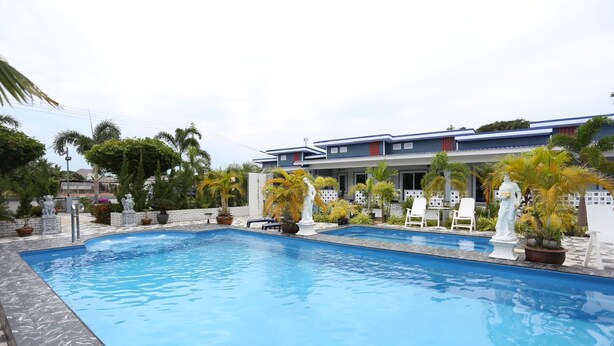 A swimming pool with lounge chairs and potted plants, surrounded by a building with a blue roof and white walls. - MB House Resort (Rayong)