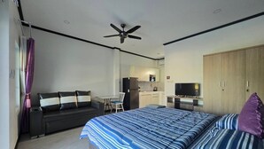 A modern bedroom with a bed, a sofa, a TV, and a kitchenette. - MB House Resort (Rayong)