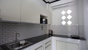 A kitchen with white cabinets, a black countertop, and a window with diamond-shaped panes. - MB House Resort (Rayong)