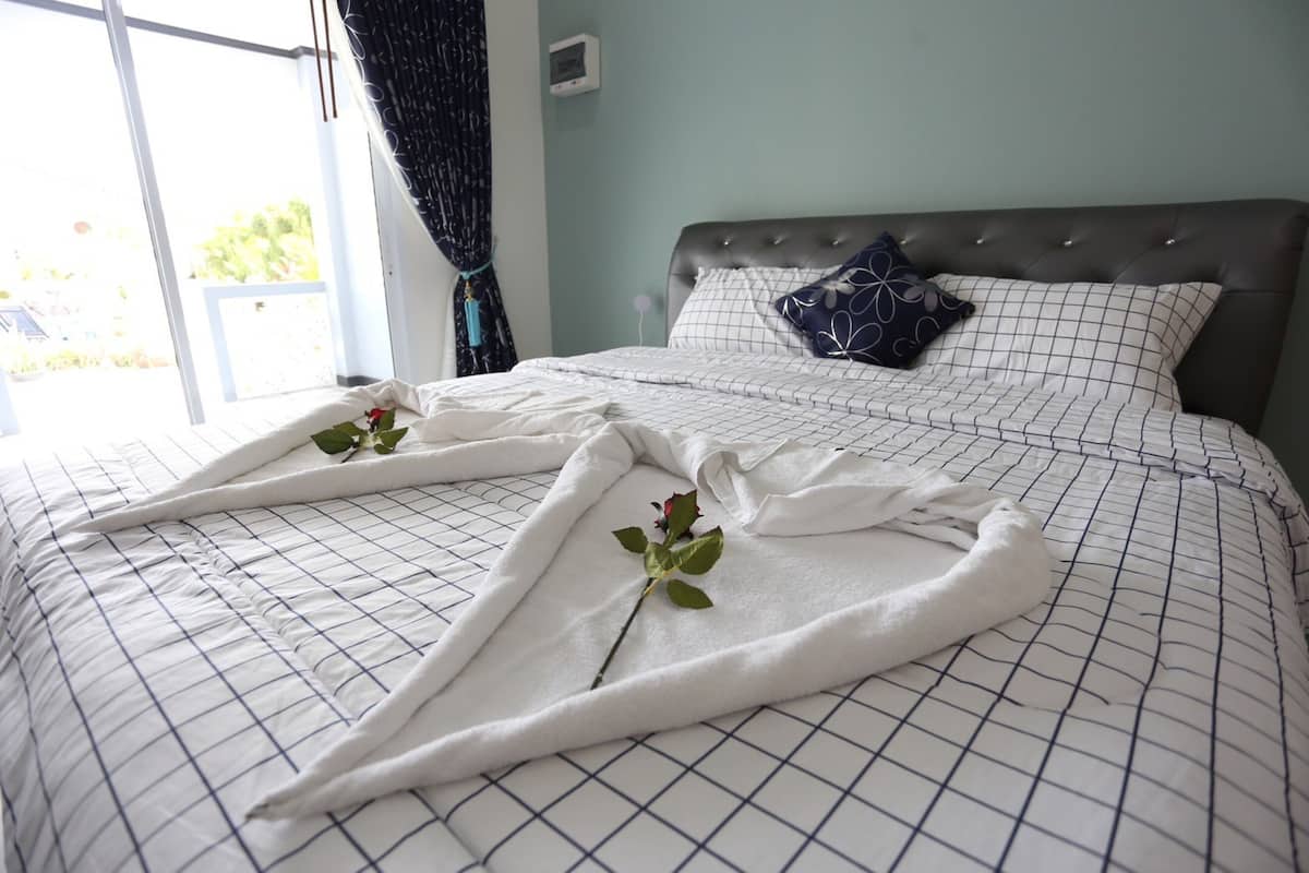 A neatly made bed with a white and blue checkered bedspread, a dark headboard, and a decorative pillow.