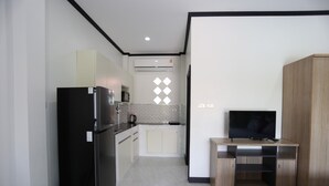 A compact kitchen with a refrigerator, microwave, and a small cabinet. There is a TV on a wooden stand and a bed with a checkered bedspread. - MB House Resort (Rayong)