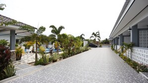 A pathway leading to a pool area with lounge chairs and potted plants. - MB House Resort (Rayong)