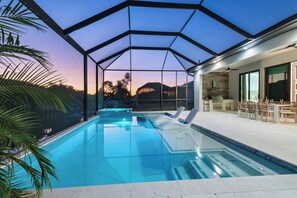 A swimming pool with a glass enclosure, lounge chairs, and a patio area with outdoor furniture. - Intervillas Florida - Villa Incredible (Cape Coral)