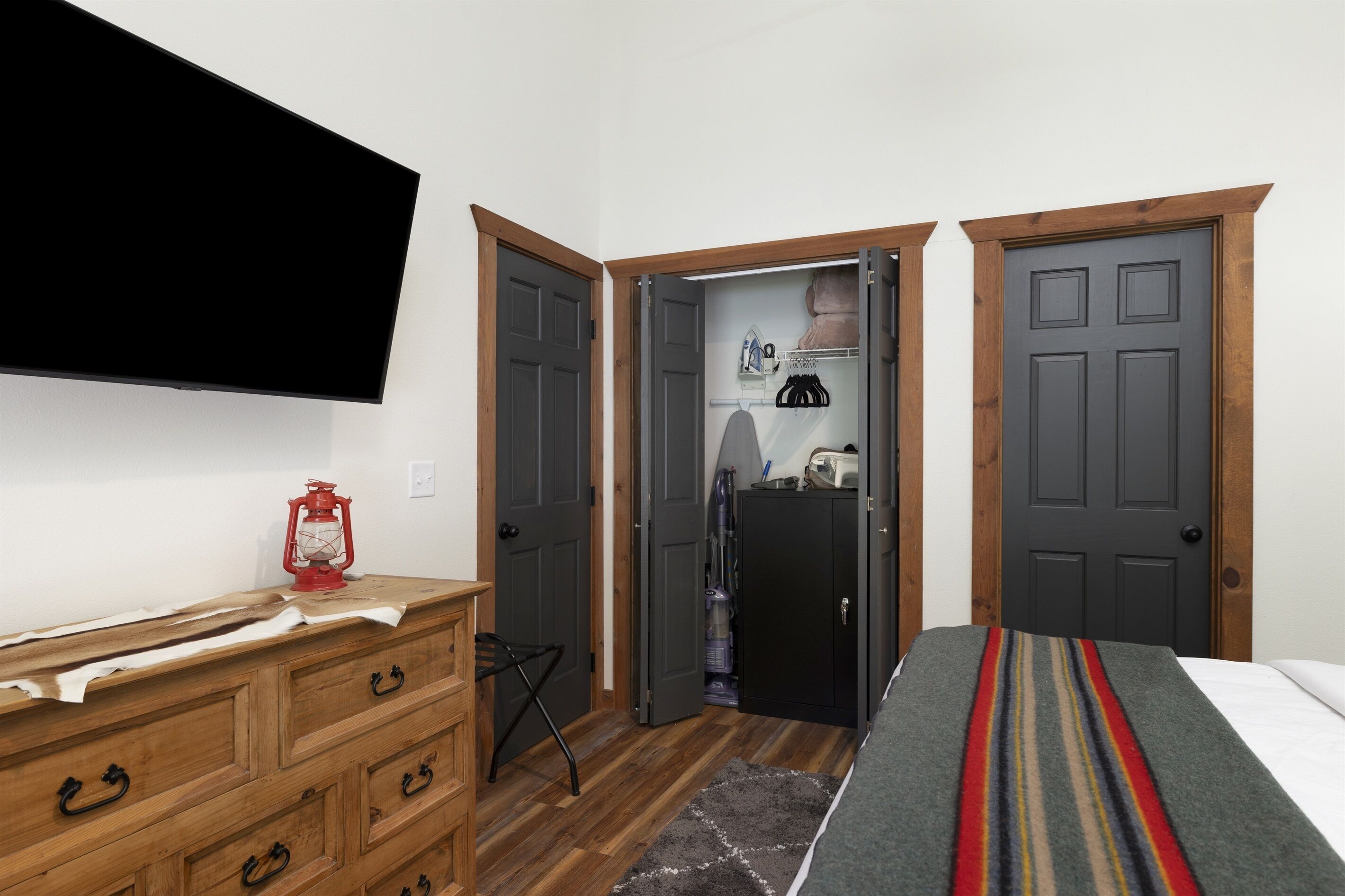 A bedroom with a bed, wooden dresser, and a TV mounted on the wall.