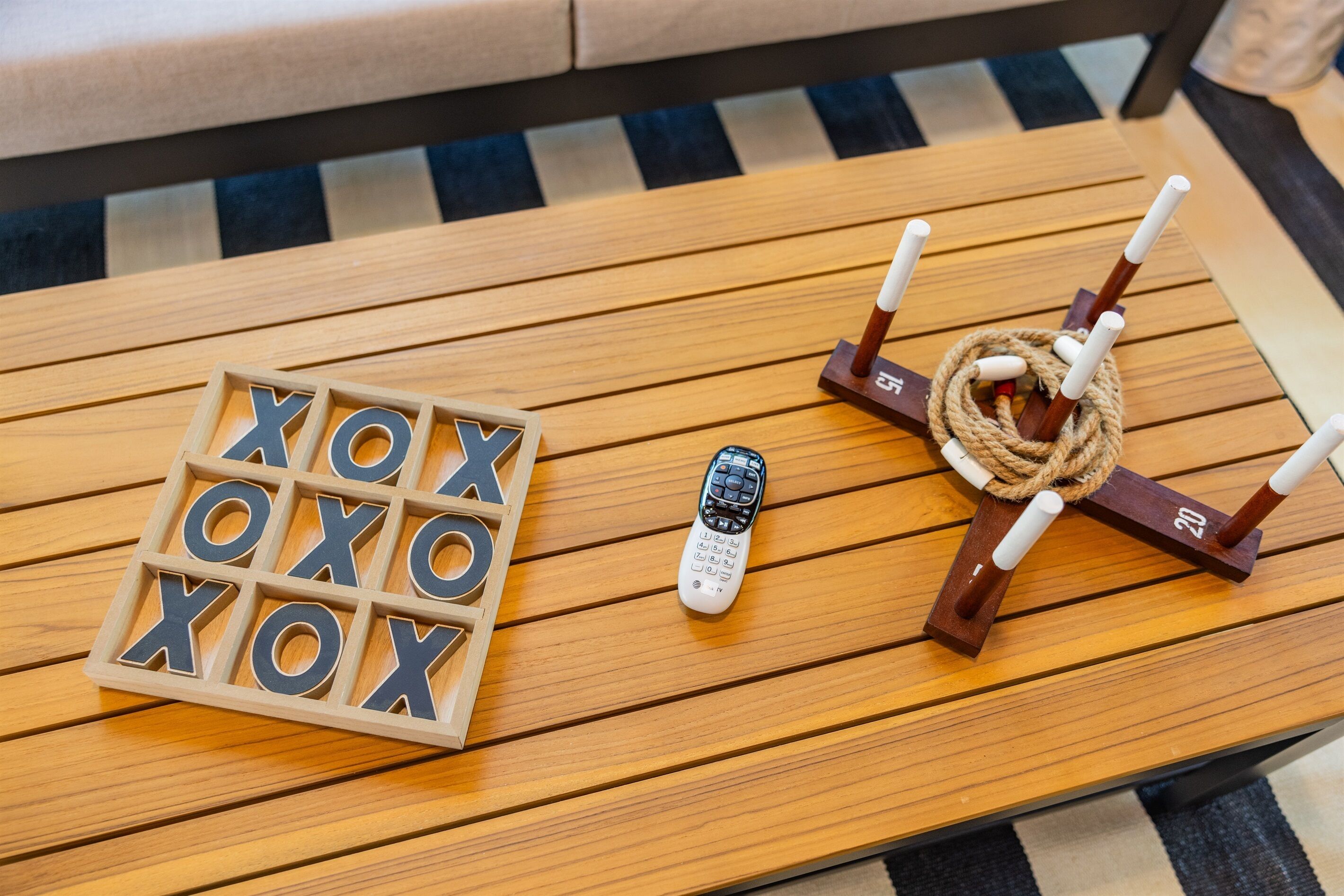 Een houten tafel met een afstandsbediening, een houten XOXO-spel en een kaarsenklem met touw.