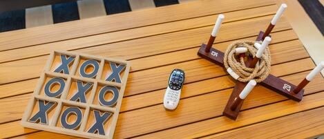 Een houten tafel met een afstandsbediening, een houten XOXO-spel en een kaarsenklem met touw.