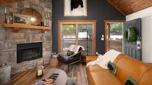 Una sala de estar acogedora con chimenea de piedra, un sofá de cuero y decoración de pared con temática de oso.