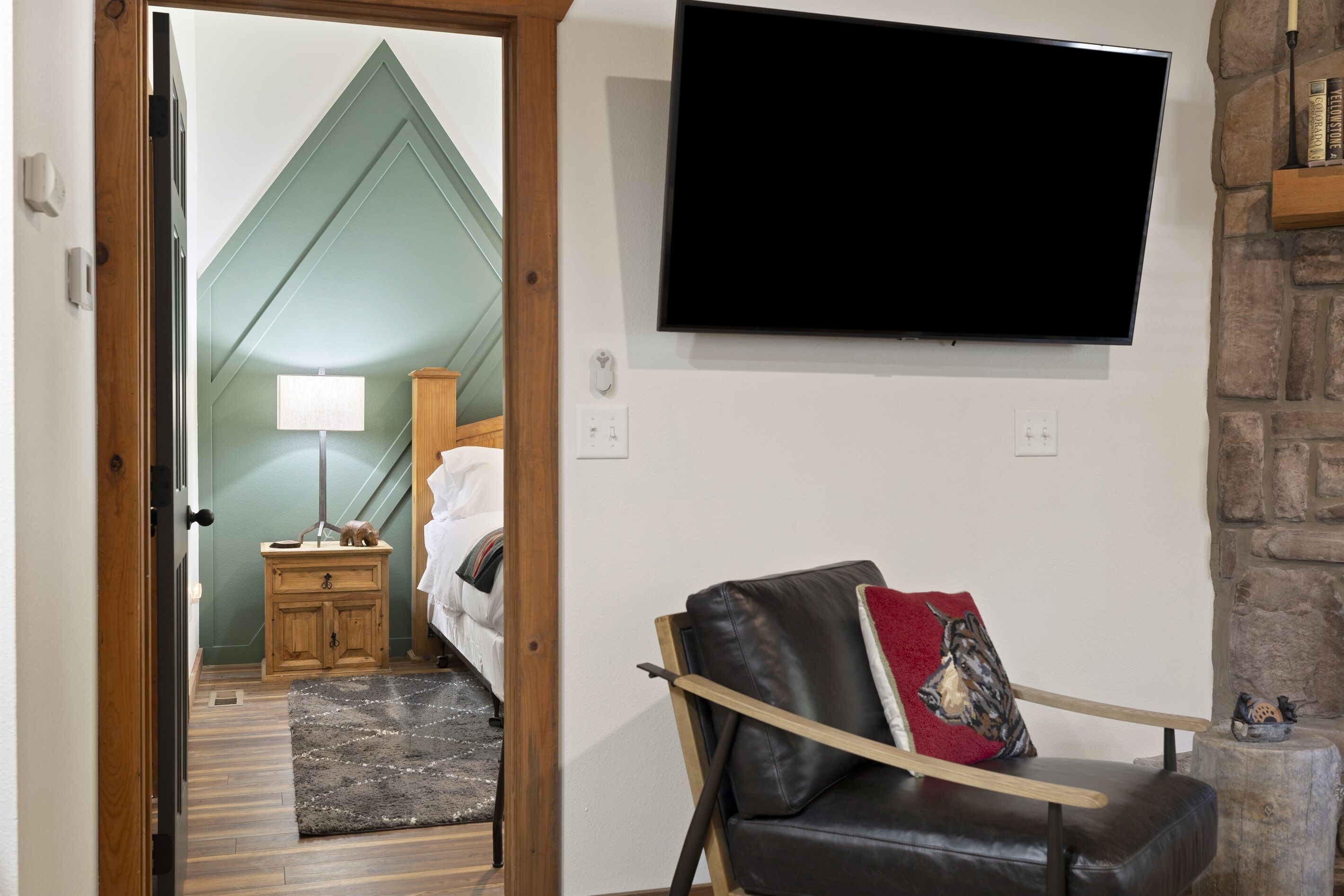 A room with a bed, a TV mounted on the wall, a wooden nightstand, and a stone wall.