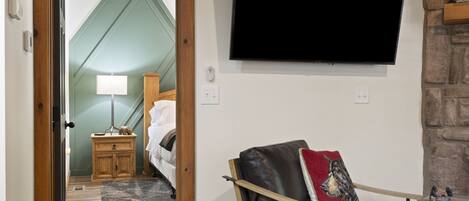 A room with a bed, a TV mounted on the wall, a wooden nightstand, and a stone wall.
