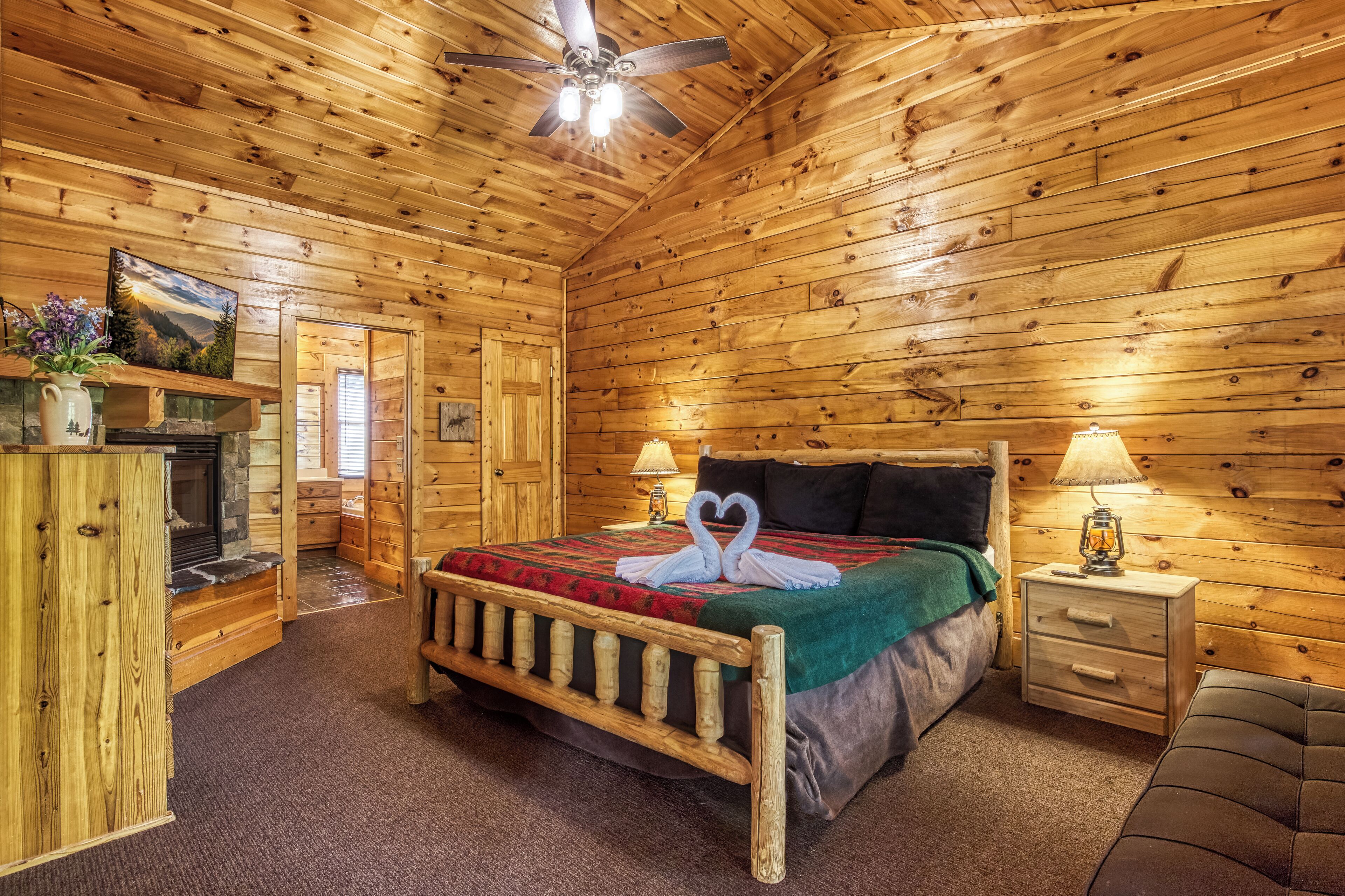 Ein Schlafzimmer einer Holzhütte mit Bett, Nachttisch, Lampe, Kamin und Deckenventilator.