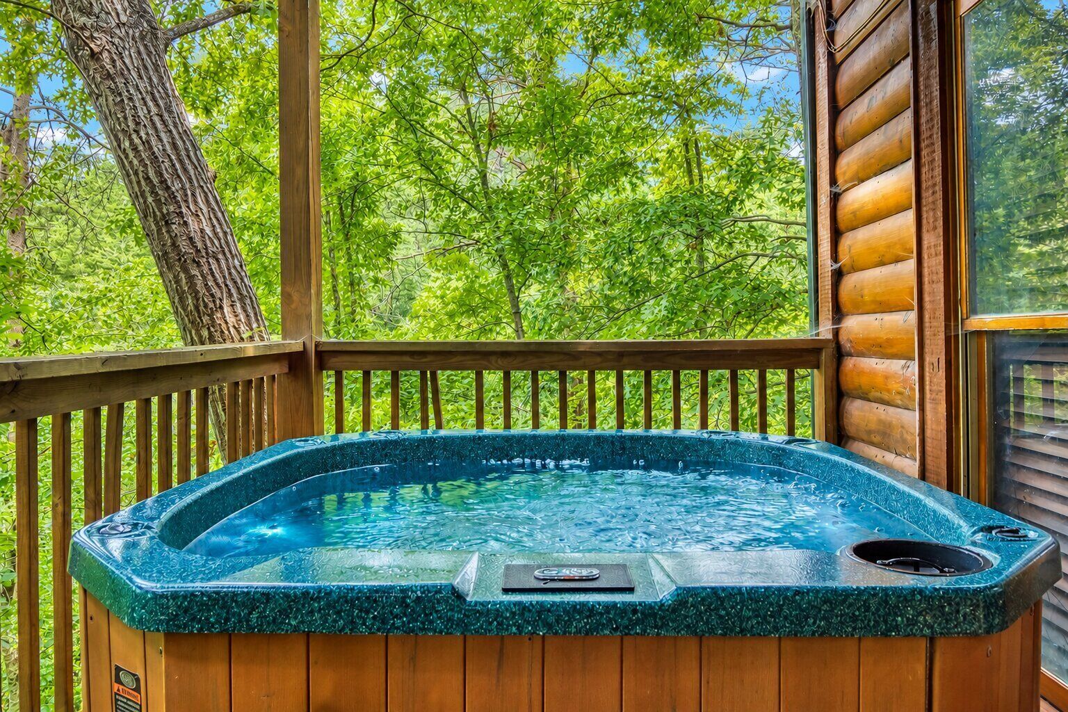 A hot tub on a wooden deck with a view of green trees.