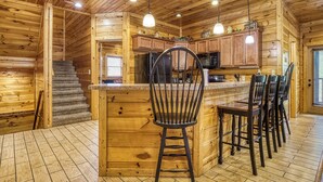 Interior de una cabaña de madera con zona de cocina, suelo de madera y barra con taburetes.