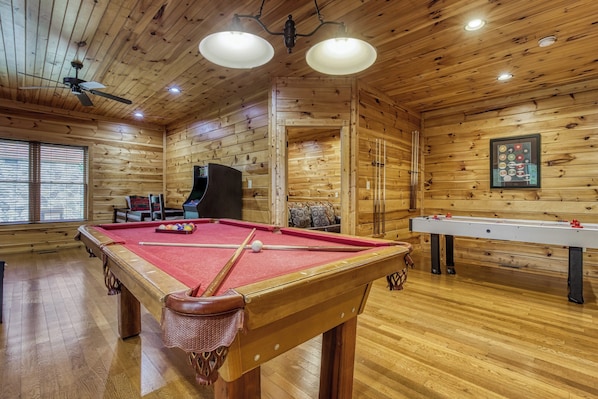 A wooden-floored room with a pool table, a foosball table, and a billiards table.