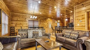 A log cabin interior with two leather sofas, a wooden coffee table, and a dining area with chairs and a table. - Gatlinburg Heights, Hot Tub, Game Room, Theater Room, FREE Attraction tickets (Gatlinburg)