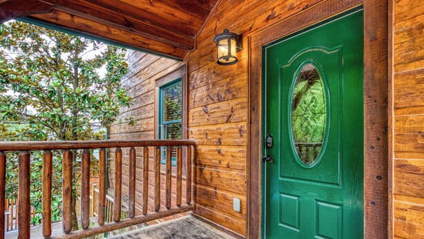 A wooden cabin with a green door, a wooden porch, and a view of trees. - Gatlinburg Heights, Hot Tub, Game Room, Theater Room, FREE Attraction tickets (Gatlinburg)