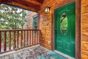 A wooden cabin with a green door, a wooden porch, and a view of trees.