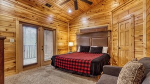 A wooden cabin bedroom with a bed, a ceiling fan, a nightstand, and a window with blinds. - Gatlinburg Heights, Hot Tub, Game Room, Theater Room, FREE Attraction tickets (Gatlinburg)