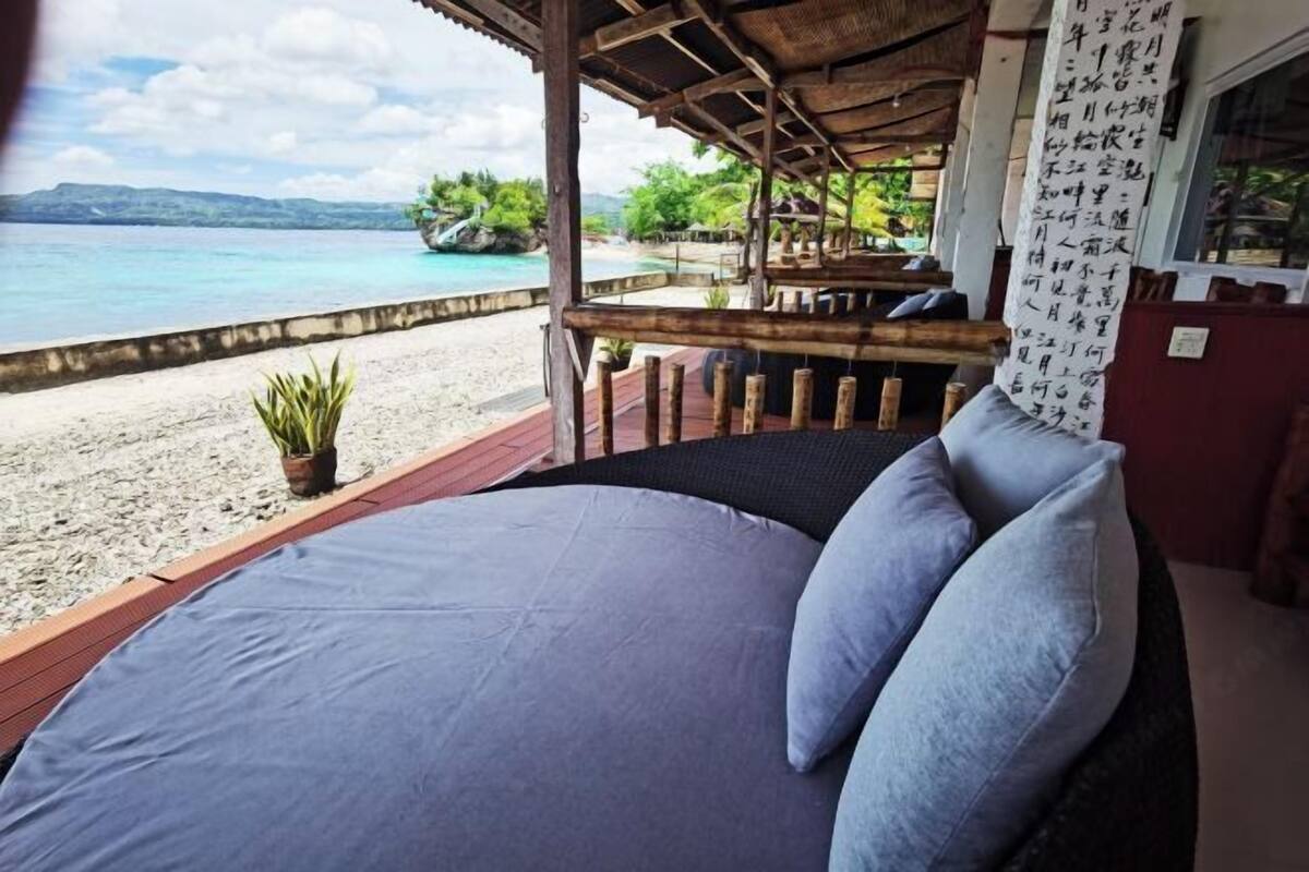 Una cama con almohadas, vista a la playa y una estructura de madera con techo de paja.