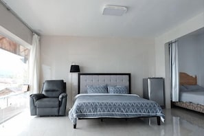 A modern hotel room with a large bed, a chair, a bedside table, a lamp, and a view of the city. - Jelly Sea Resort (Siquijor Island)