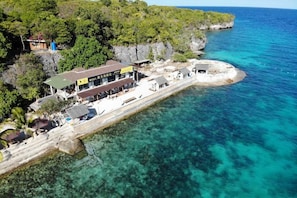 An aerial view of a coastal hotel with a pier extending into clear blue waters, surrounded by lush greenery and rocky cliffs. - Jelly Sea Resort (Siquijor Island)