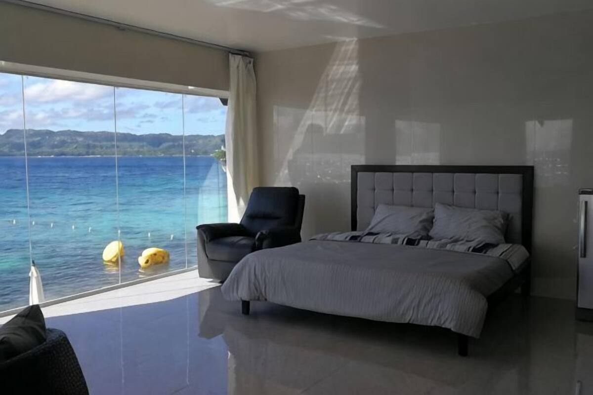 Un dormitorio con una ventana grande, una cama, una silla y vista al mar.
