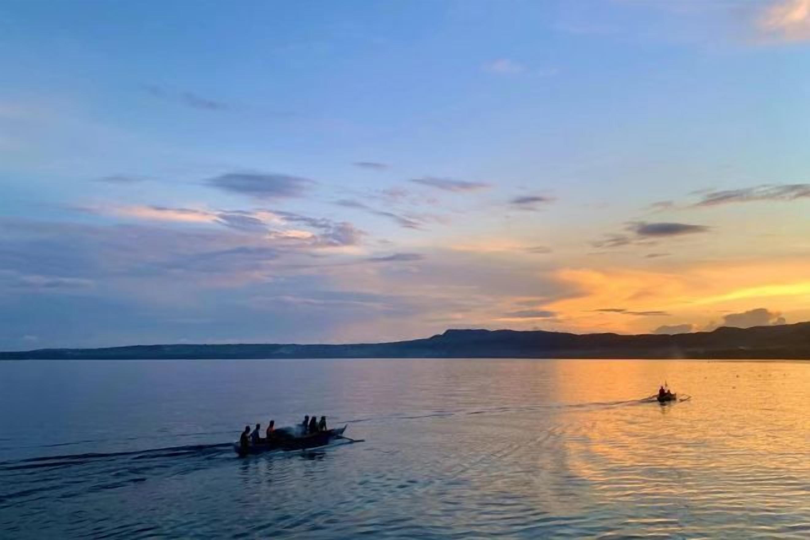 A calm lake with a boat carrying people, surrounded by a clear sky.