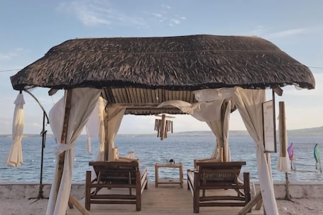 A beachside gazebo with a thatched roof, wooden benches, and a view of the sea.. Jelly Sea Resort