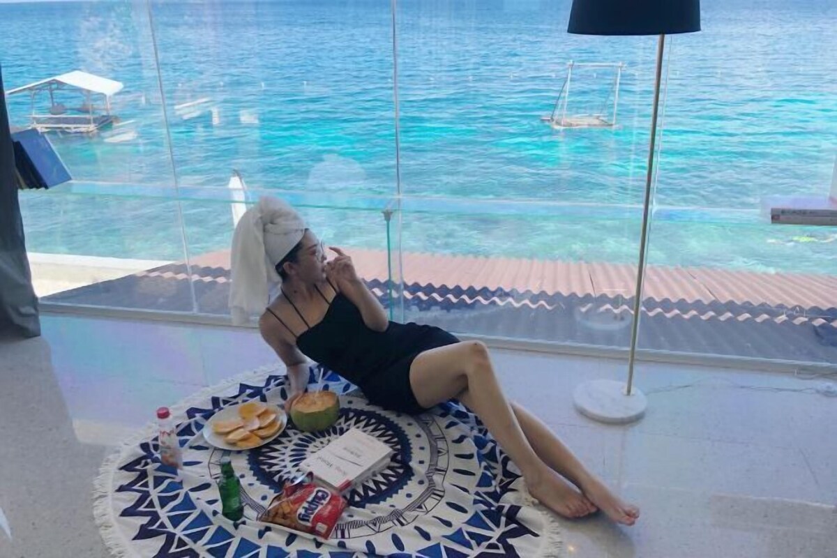 A person relaxing on a patterned mat by a window overlooking a body of water.