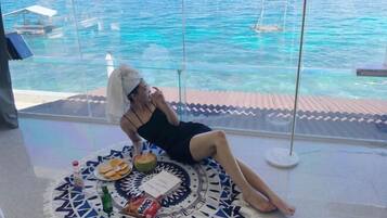 A person relaxing on a patterned mat by a window overlooking a body of water.