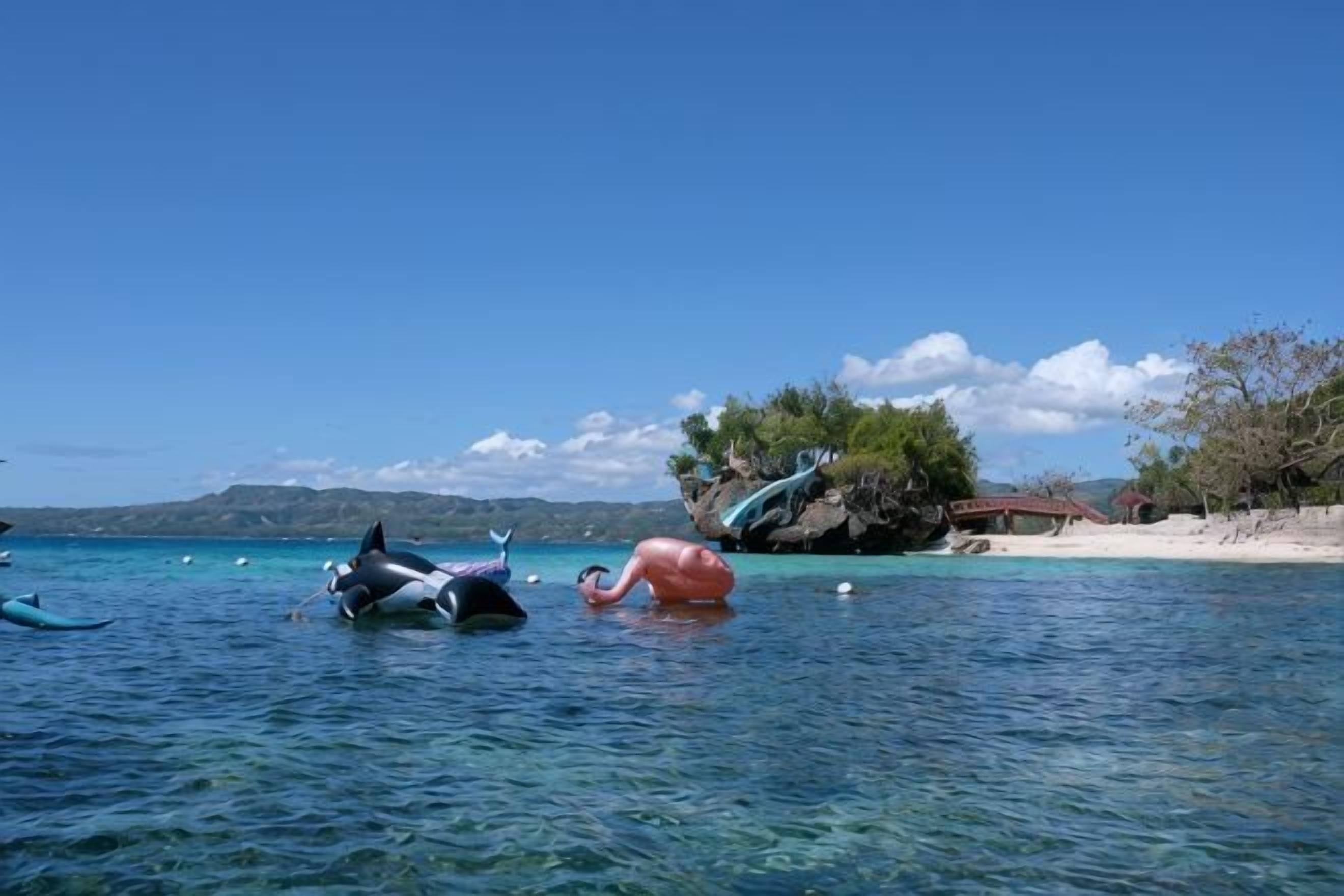 A clear blue sea with boats and a rocky island in the background.