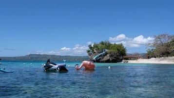 A clear blue sea with boats and a rocky island in the background.